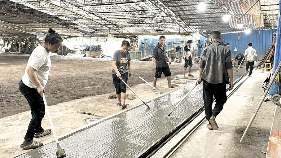 ●經過反覆浸染和日曬加工的坯綢在機器輔助下「鋪」上河泥，工人們正在消除坯綢表面的河泥氣泡。