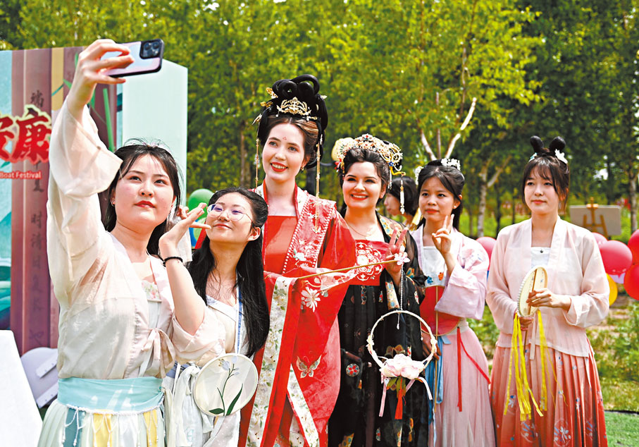 ●越來越多的外國朋友來到中國、看見中國、感受中國、了解中國。圖為兩位外國人和中國女孩通過穿漢服體驗端午節習俗。 資料圖片