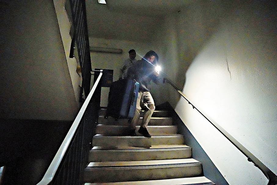 ●希思羅機場旅客開啟手機電筒,提着行李落樓梯。 美聯社