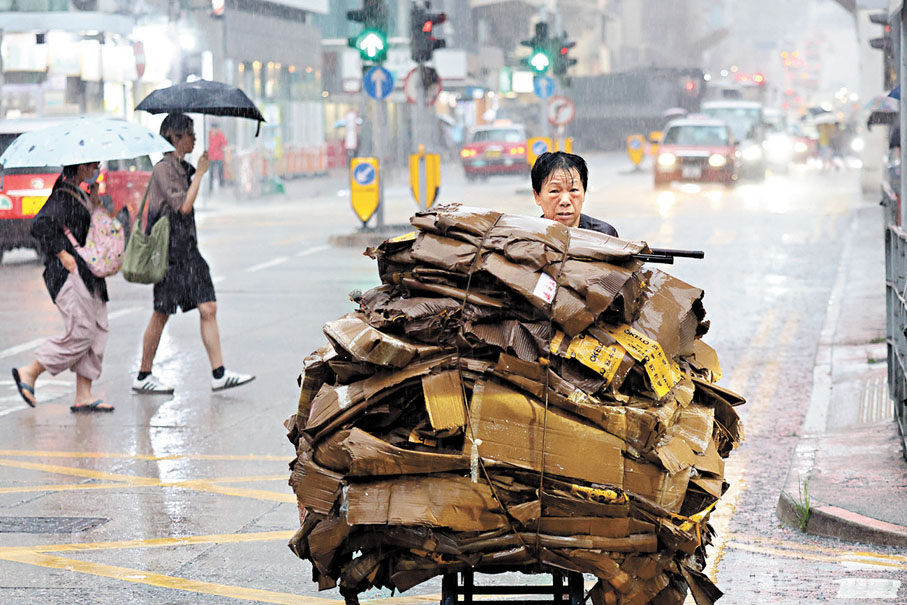 ● 工友冒着暴雨推着山一般的紙皮。  香港文匯報記者北山彥  攝
