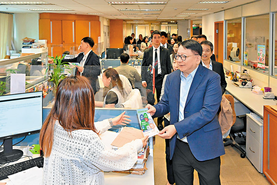 ●陳國基(右)在土地註冊處同事的工作間向他們派發選民登記宣傳單張。