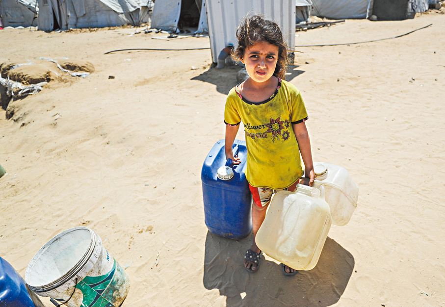 ●一名流離失所的巴童在加沙城附近等待領水。 新華社