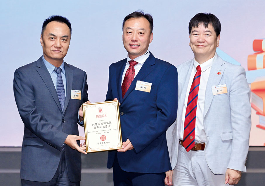 ●中央政府駐港聯絡辦社團聯絡部副部長余學傑（左）、香港客屬總會常務副主席兼秘書長黃敬（右）向支持機構之一「大灣區共同家園青年公益基金」致送感謝狀，該會行政總裁楊彬（中）代表接受。