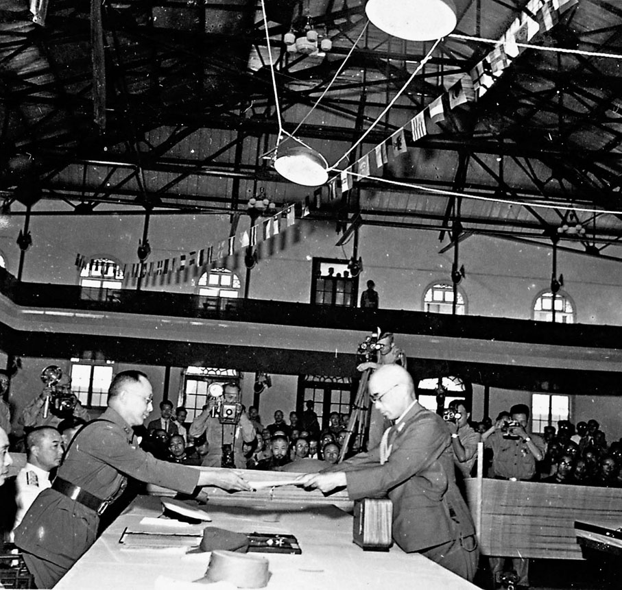 ●1945年9月9日，駐華日軍最高指揮官陸軍大將岡村寧次在南京簽署降書後，由參謀長小林淺三郎（右）向國民黨陸軍一級上將何應欽（左）呈交。 資料圖片