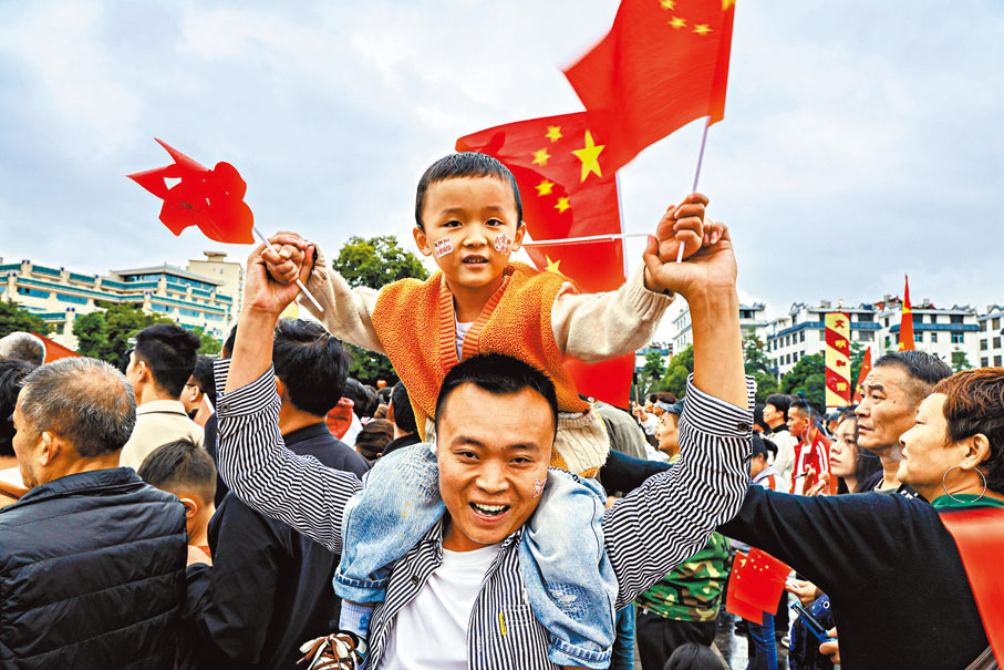 【雲南】10月1日，一對父子在雲南省曲靖市麒麟區南城門廣場觀看升旗。     新華社