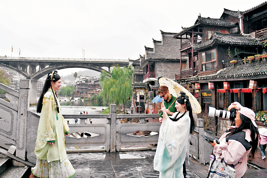 ●李書磊在近日出版的《〈中共中央關於制定國民經濟和社會發展第十五個五年規劃的建議〉輔導讀本》中，發表署名文章《激發全民族文化創新創造活力》。圖為11月6日，外國遊客身着「中國風」服裝在鳳凰古城拍照、遊玩。 新華社