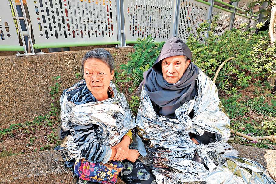●余太與99歲丈夫由街坊攙扶落樓逃生後，披着錫紙保暖。 香港文匯報記者劉友光  攝