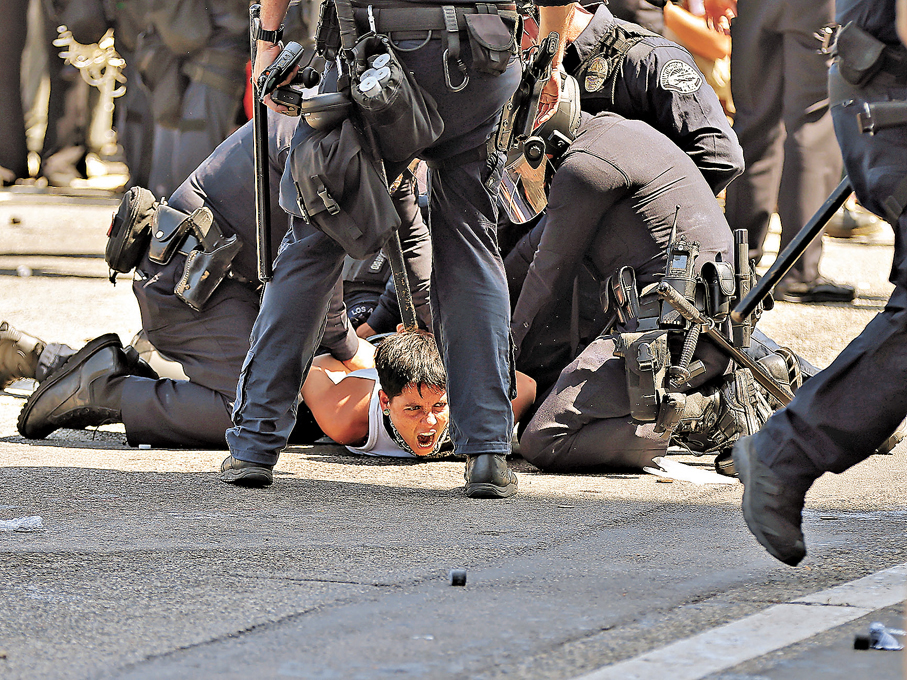 ● 近年美國社會因政治動盪、生活成本飆升及社會權益受限，引發大規模公民出走現象。圖為一名抗議者被警察制服。 資料圖片