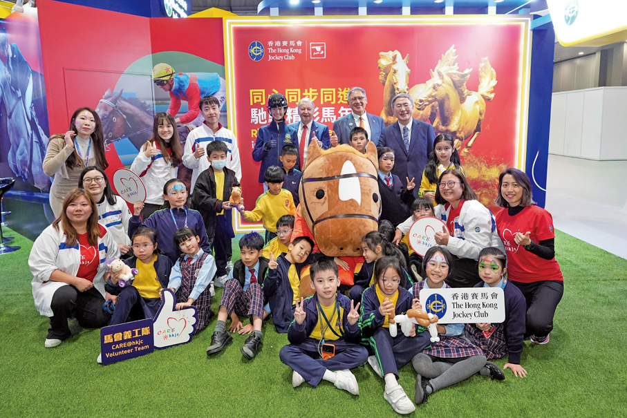 ▲香港特區政府政務司副司長卓永興（後排右一）、馬會副主席兼浪琴香港國際馬術盛典主席及中國香港馬術總會會長黃嘉純（後排右二）、馬會行政總裁應家柏（後排右三）及馬會青少年馬術隊成員王嘉莉（後排右四），與馬會義工隊及進場觀賽的青年及基層團體於馬會互動攤位合照。