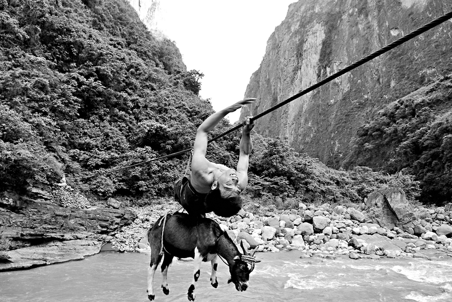 ●早前，阿布洛哈村村民們出村需通過50多米長的溜索跨河到對岸。圖為2005年阿布洛哈村村民背着羊過溜索。 資料圖片