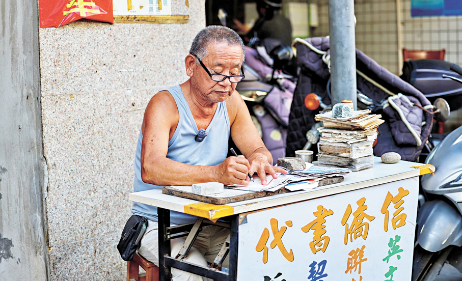 ●姜明典多年來靠這樣簡陋的攤子，替無數番客嬸寫了十餘萬封家書，勾連起家庭生活和無數的牽掛。香港文匯報石獅傳真