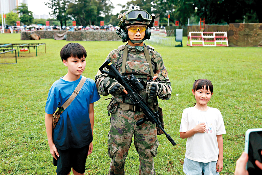 ●謝小朋友（左）和妹妹與全副武裝的駐港部隊官兵合照。 香港文匯報記者黃艾力 攝