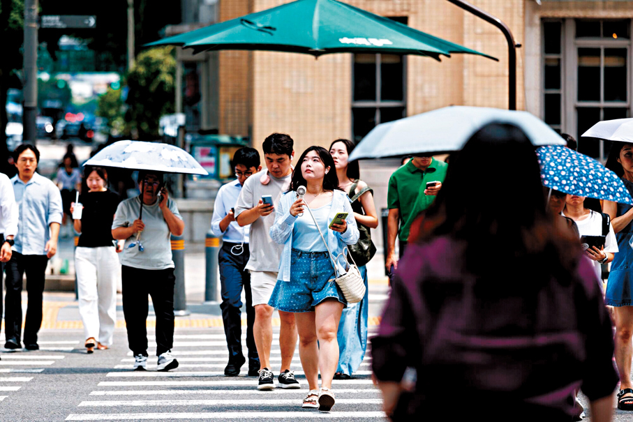 ●首爾民眾在街上手持小風扇消暑。 彭博社