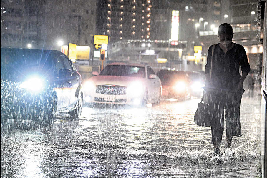 ●一名女子在大雨下索性放棄擔遮，提起褲管涉水而行。 法新社