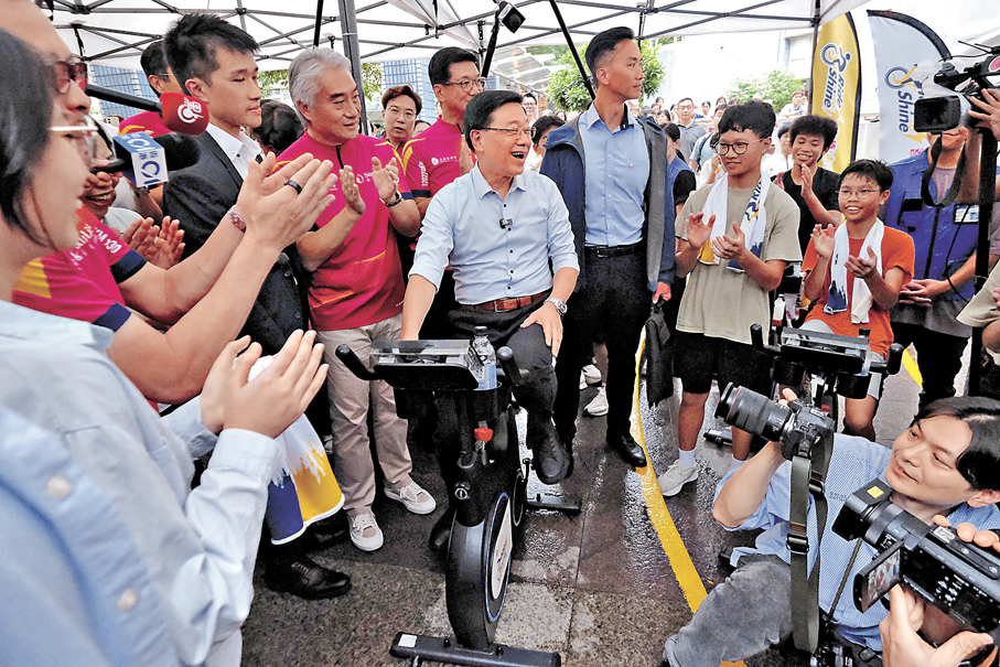 ●李家超在學生邀請下試踩智能健身單車。香港文匯報記者涂穴  攝