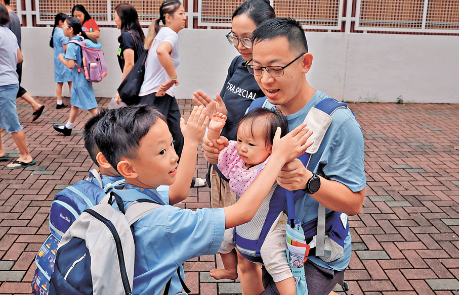 ●學童在校門前與父母及年幼妹妹「擊掌」道別。 