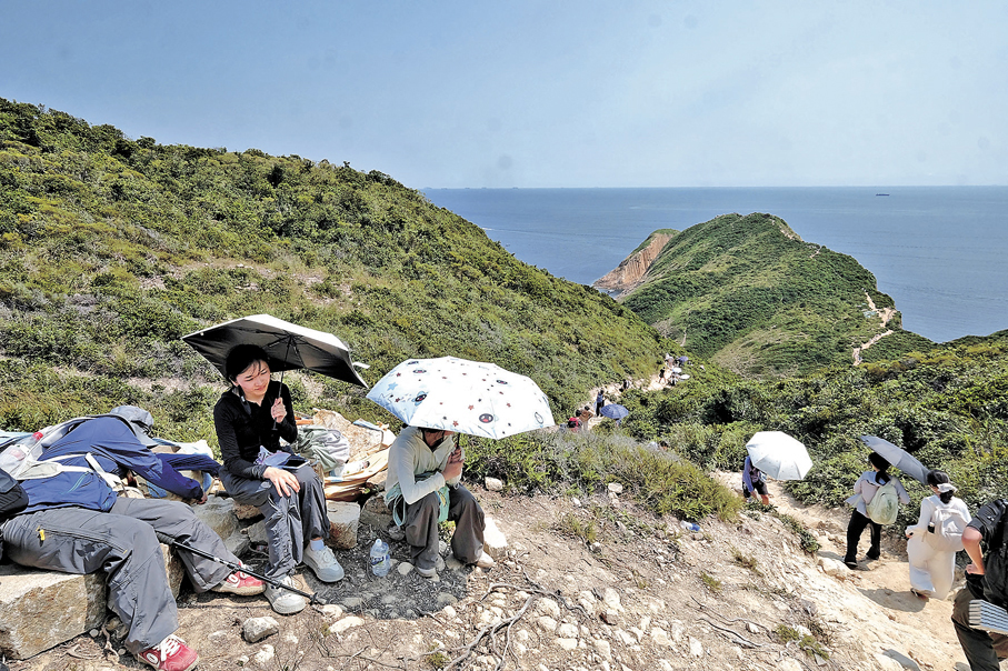 ●昨日天氣酷熱，不少到西貢破邊洲行山的旅客均帶備雨傘防曬。 香港文匯報記者涂穴  攝